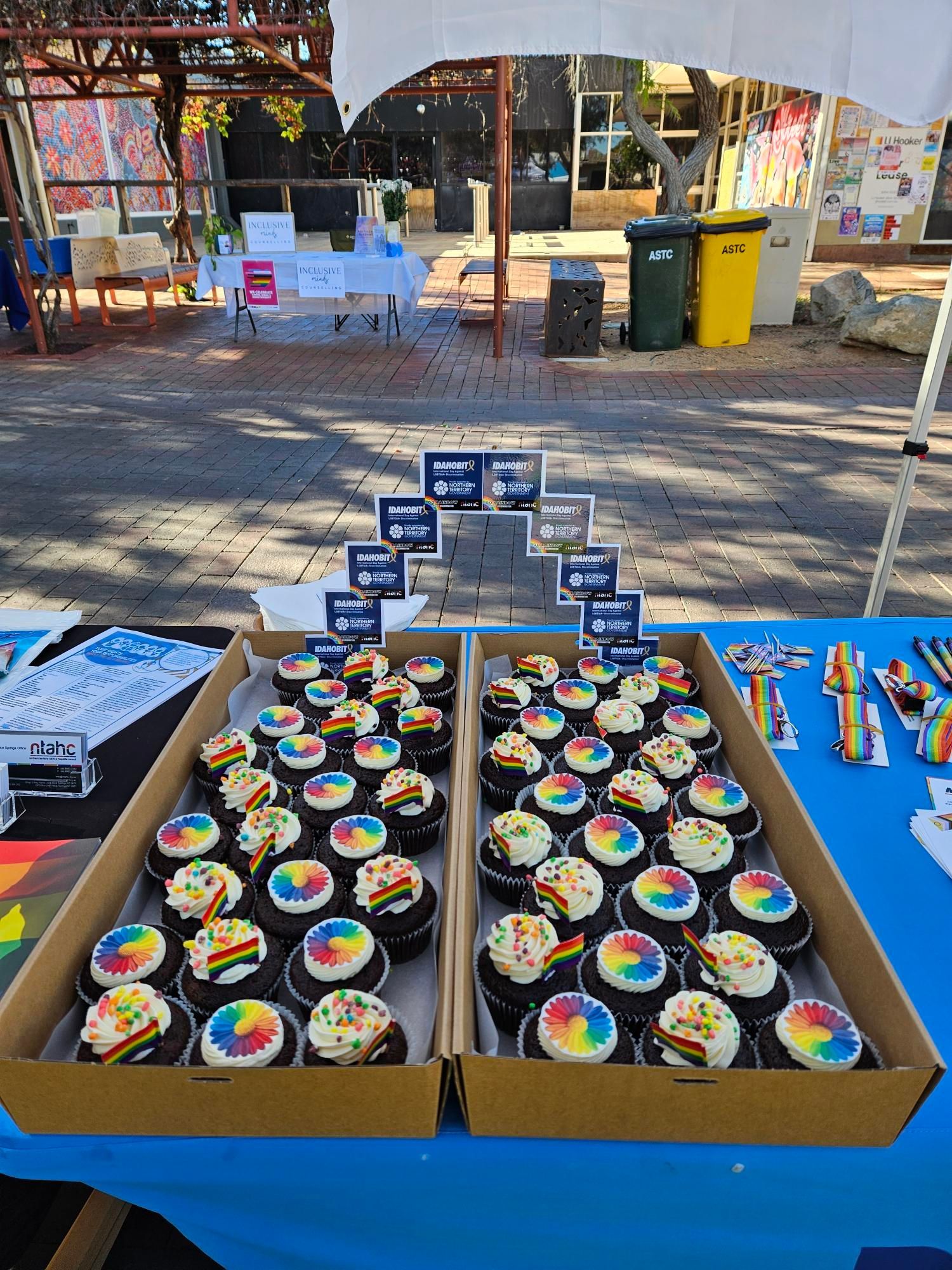 Two boxes of cupcakes with rainbow frosting are sitting on a table.