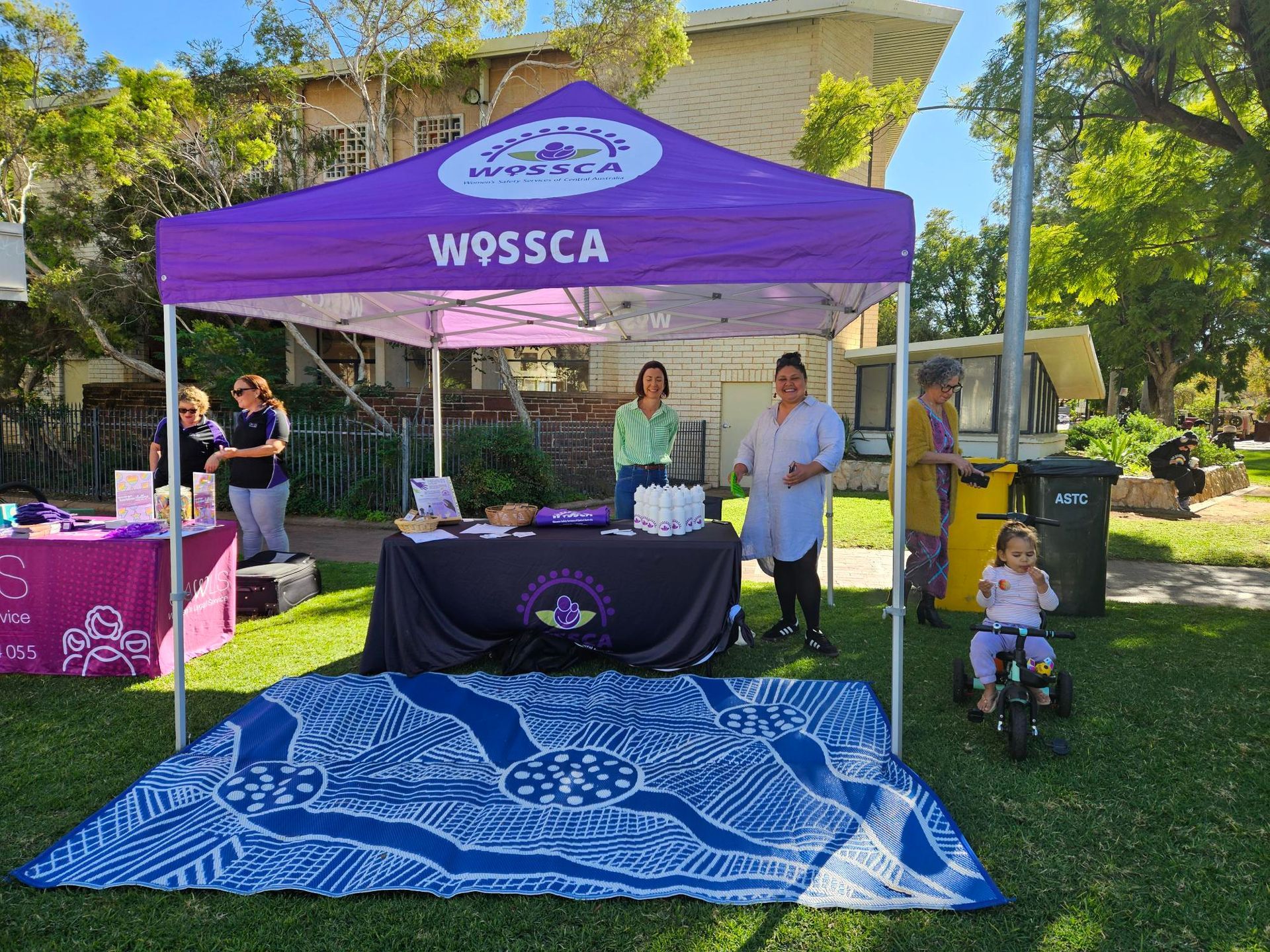 A group of people are standing under a purple tent in a park.