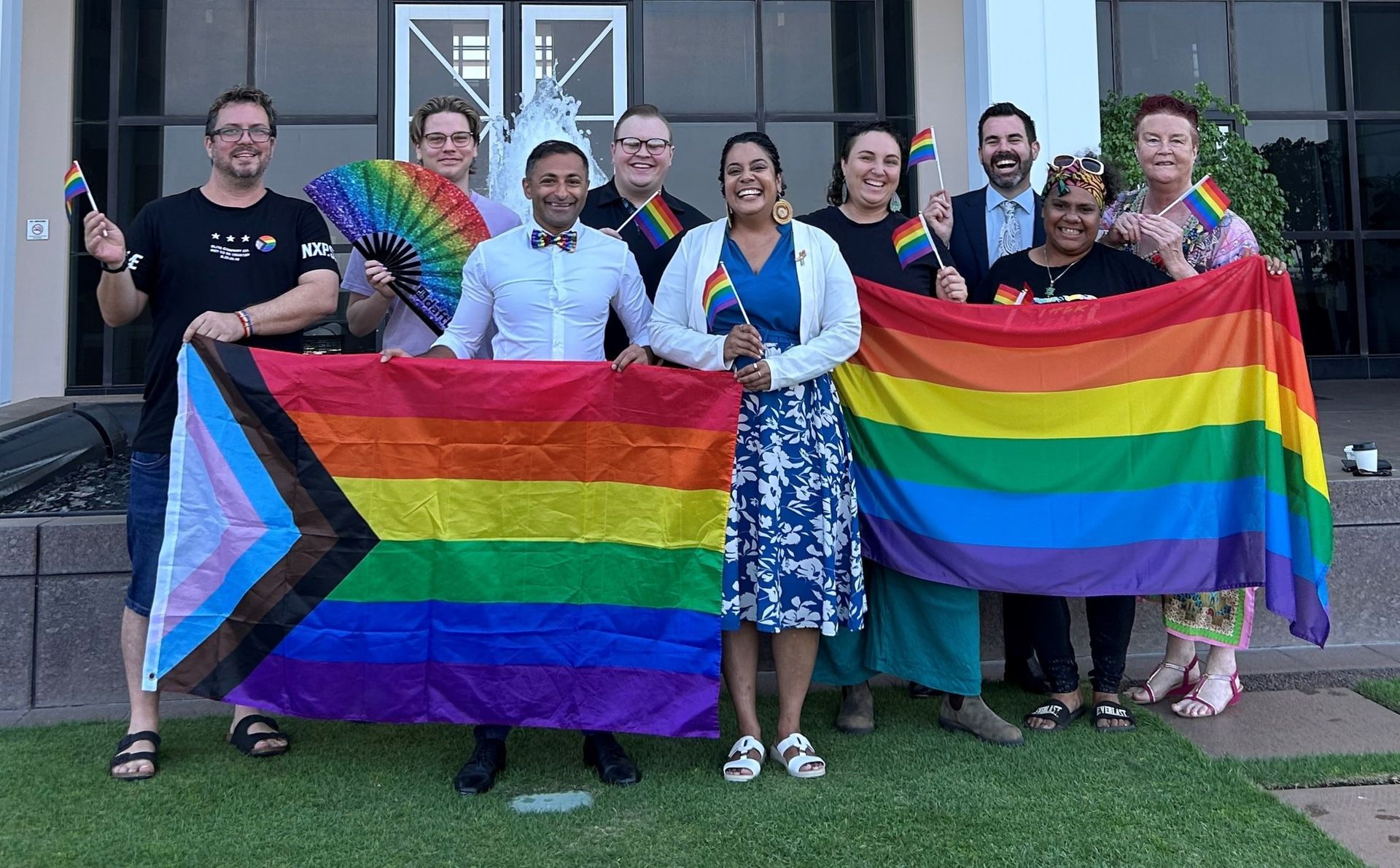 A group of people are holding rainbow flags in front of a building.