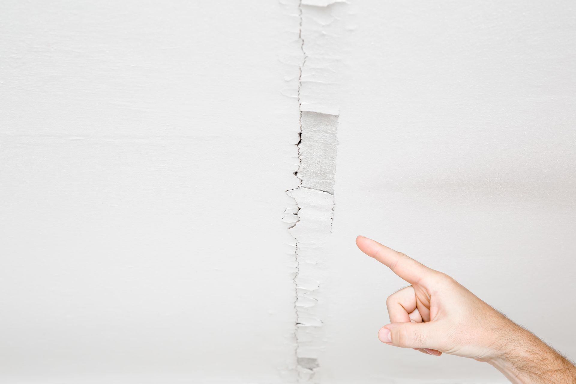 White ceiling with a vertical crack; a hand pointing at the damage.