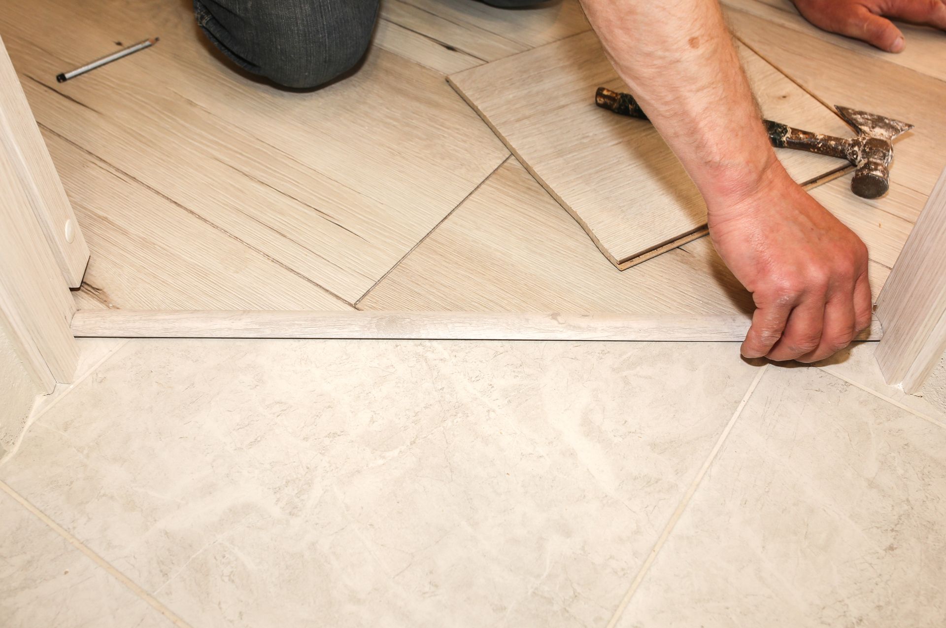 Person installs floor tiles, using a hammer, in a doorway.