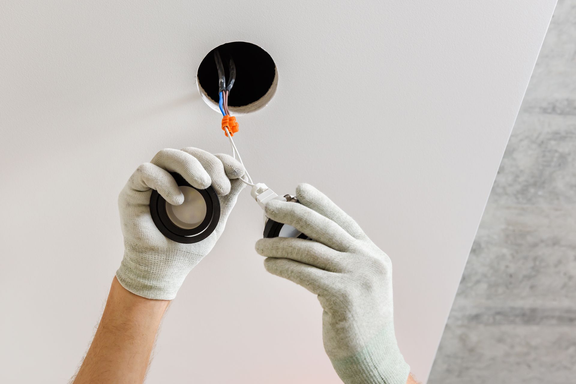 Person in gloves installing wiring, reaching towards a ceiling fixture hole.