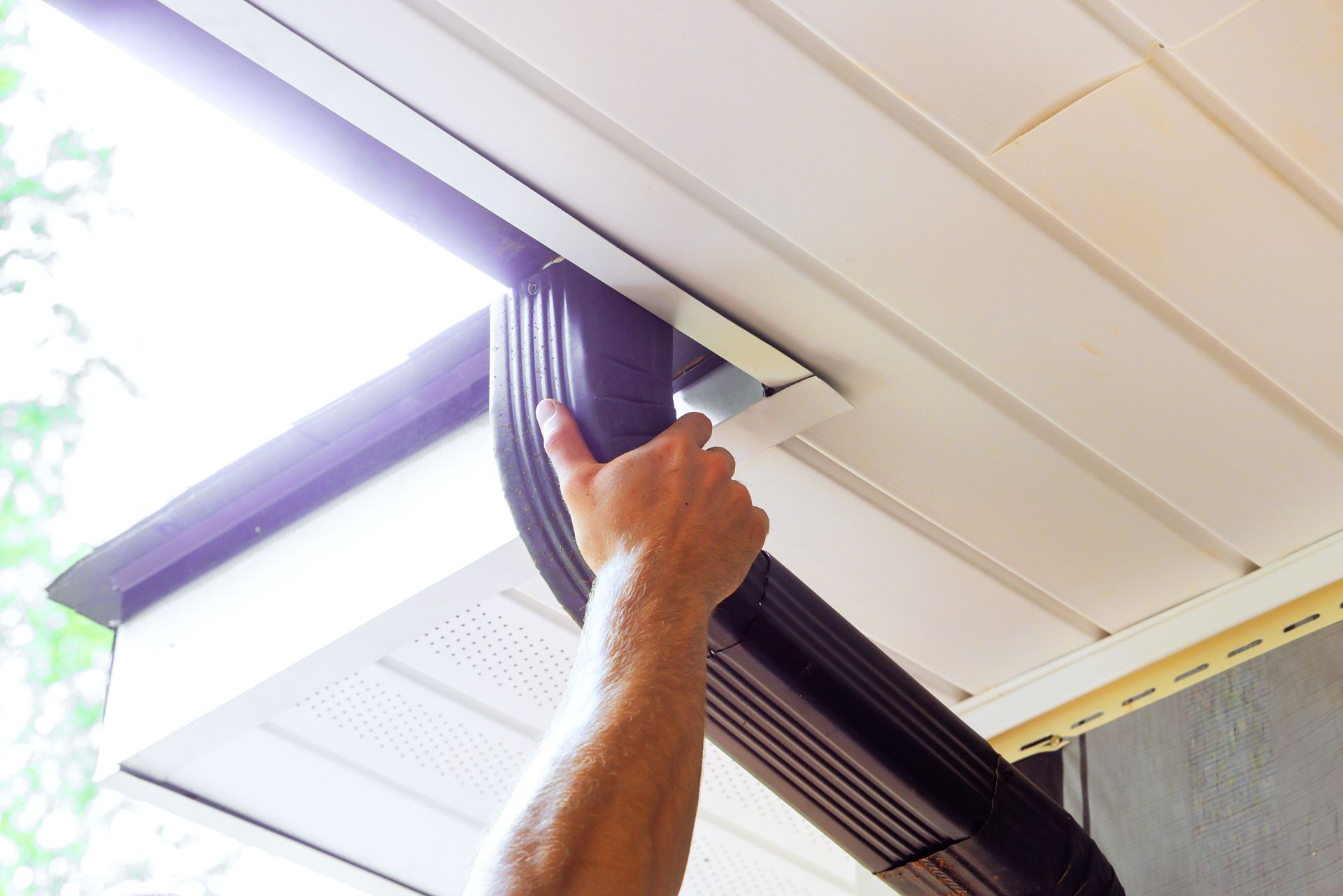 Person installs a black gutter on a white building's edge.