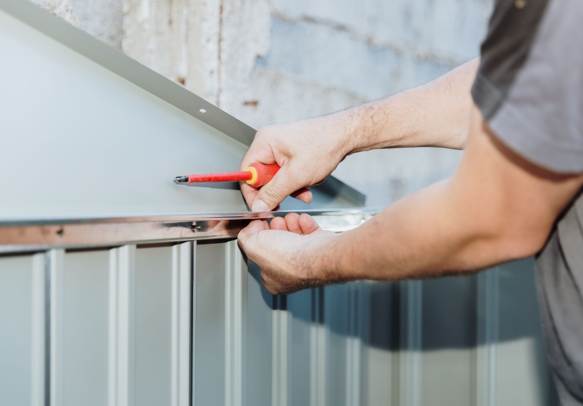 Person using a screwdriver to attach a metal panel to a structure.