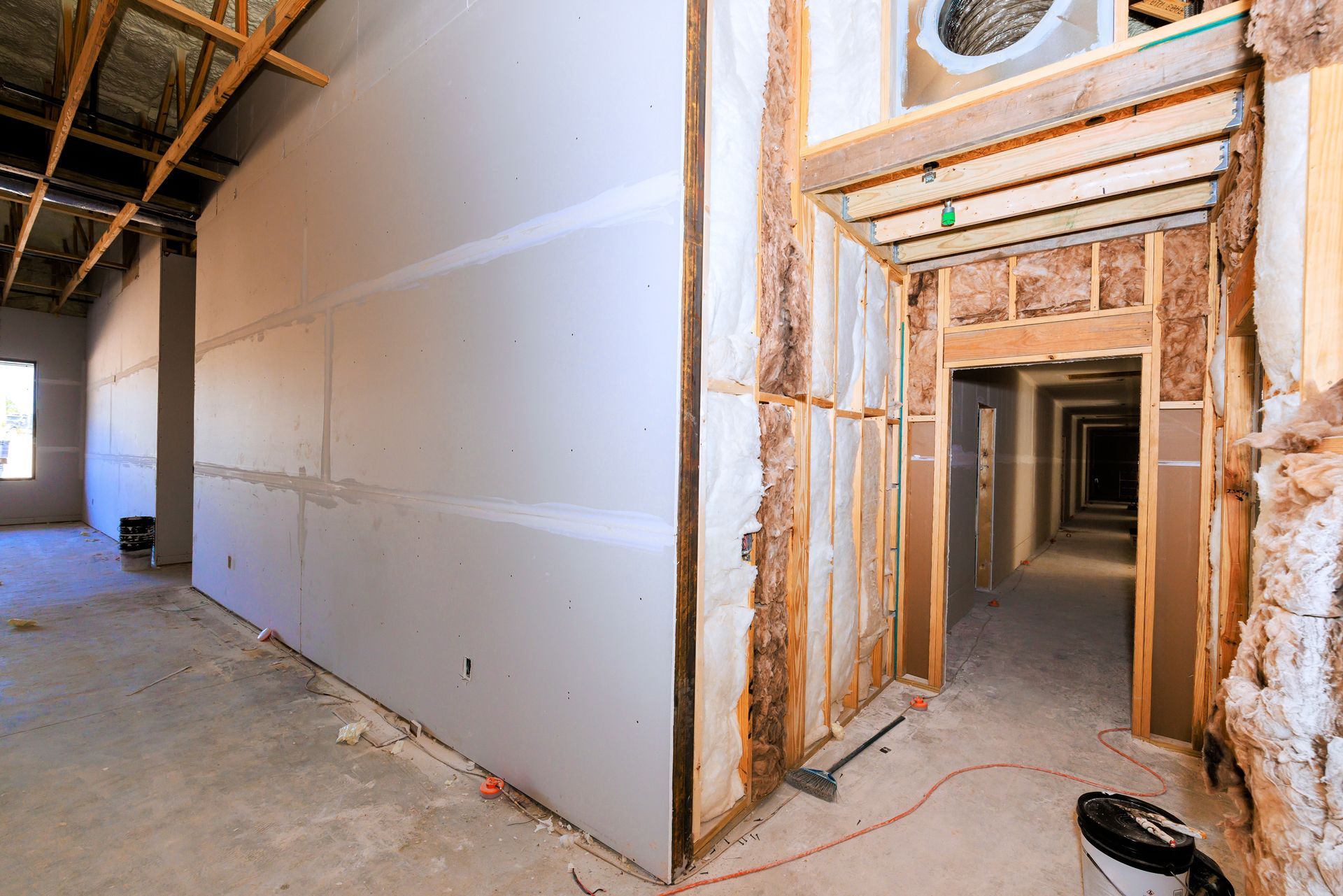 Interior view of a building under construction, showing drywall and exposed wooden framing.