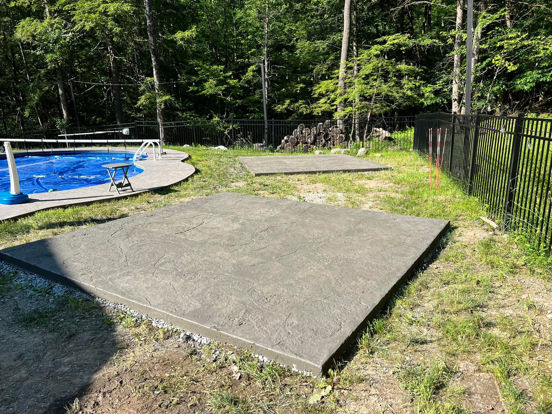 A concrete patio in a backyard next to a pool.