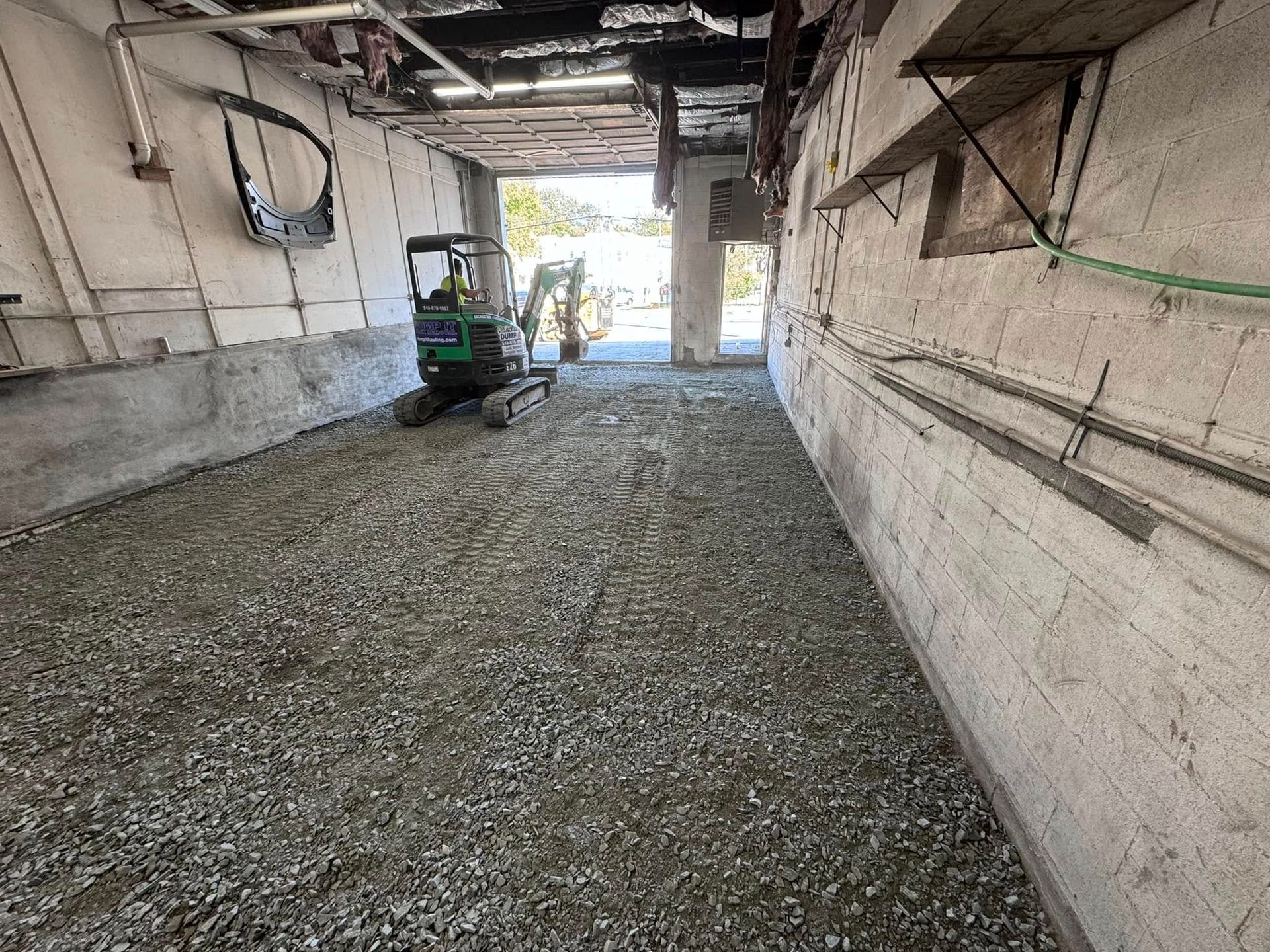 A green excavator is sitting in the middle of a garage.