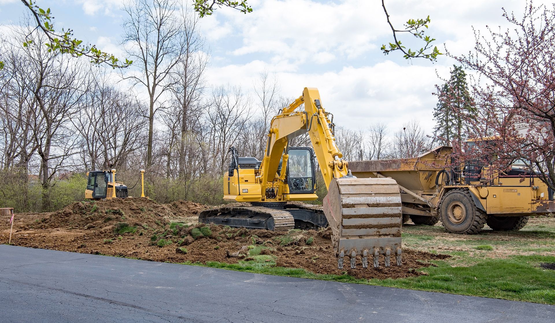 A yellow excavator is sitting on the side of the road next to a dump truck.