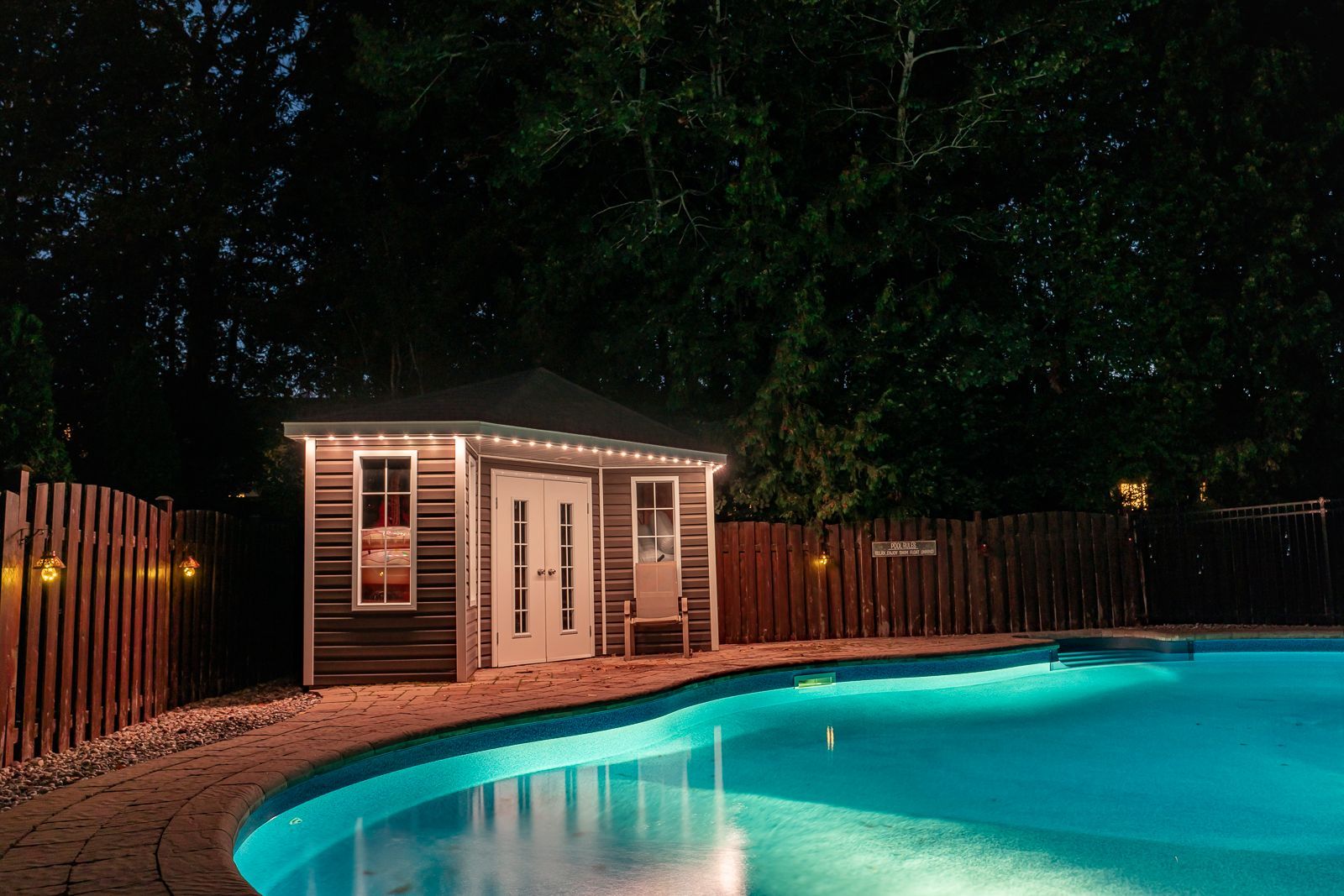 A swimming pool with a house in the background at night.
