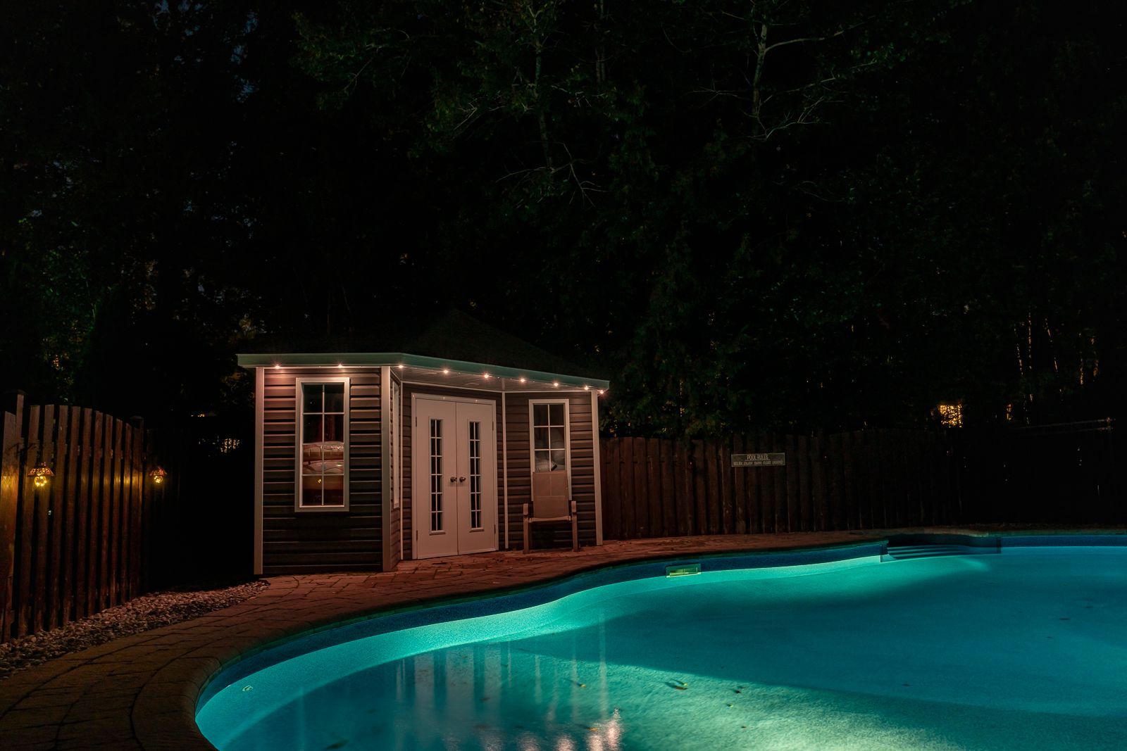 A swimming pool is lit up at night with a shed in the background.