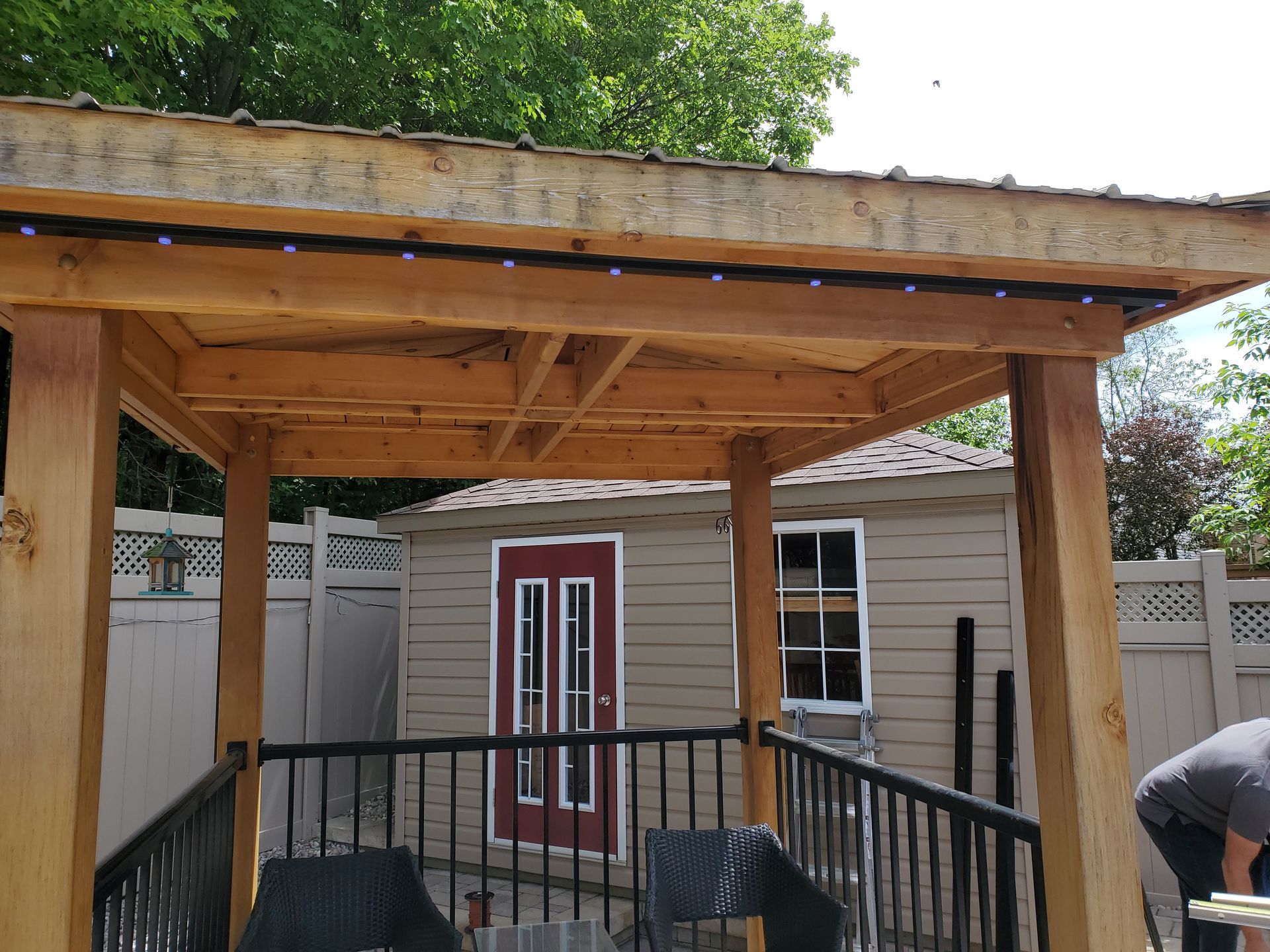 A man is working on a wooden gazebo in front of a house.