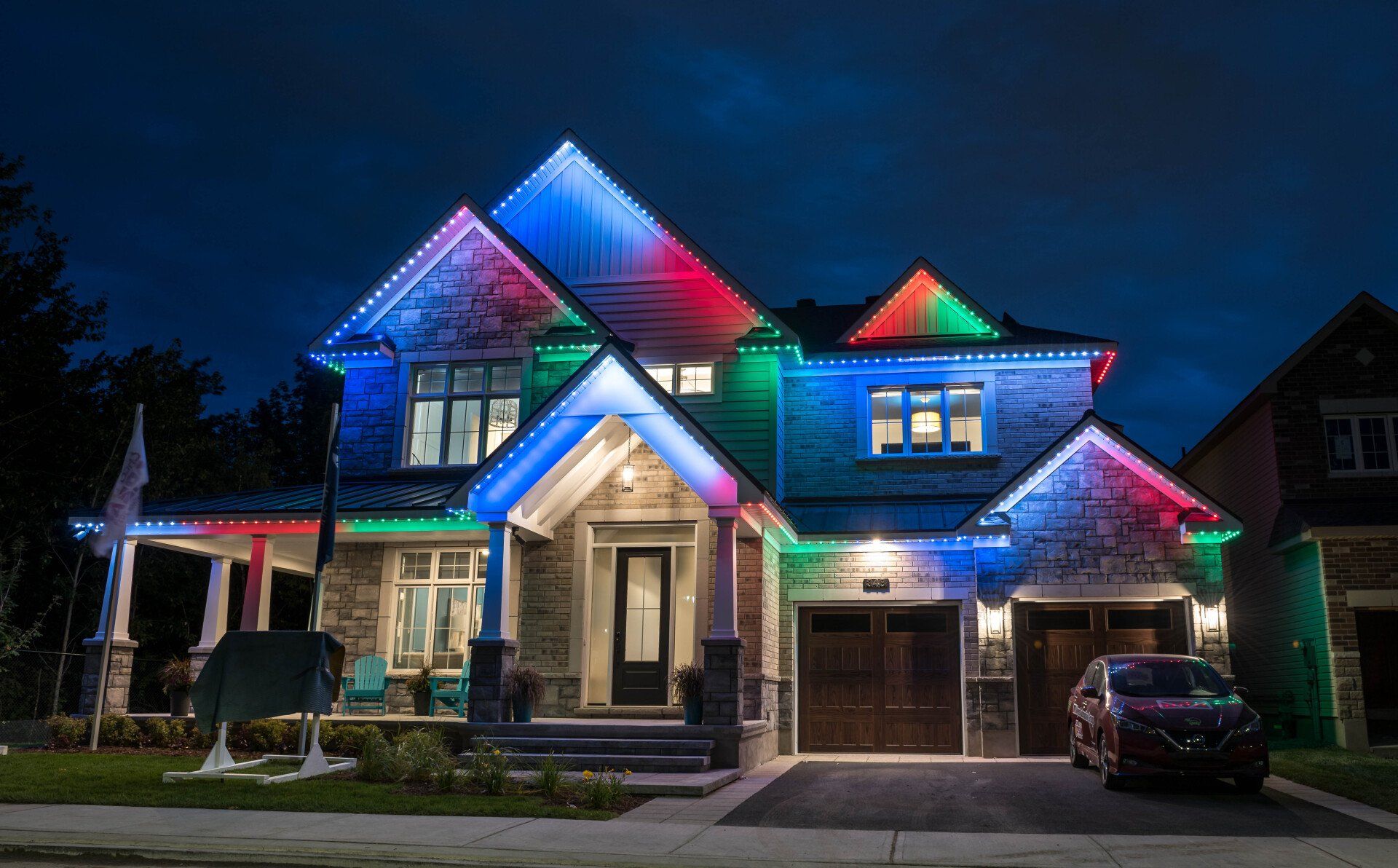 A house with a car parked in front of it is lit up with colorful lights at night.