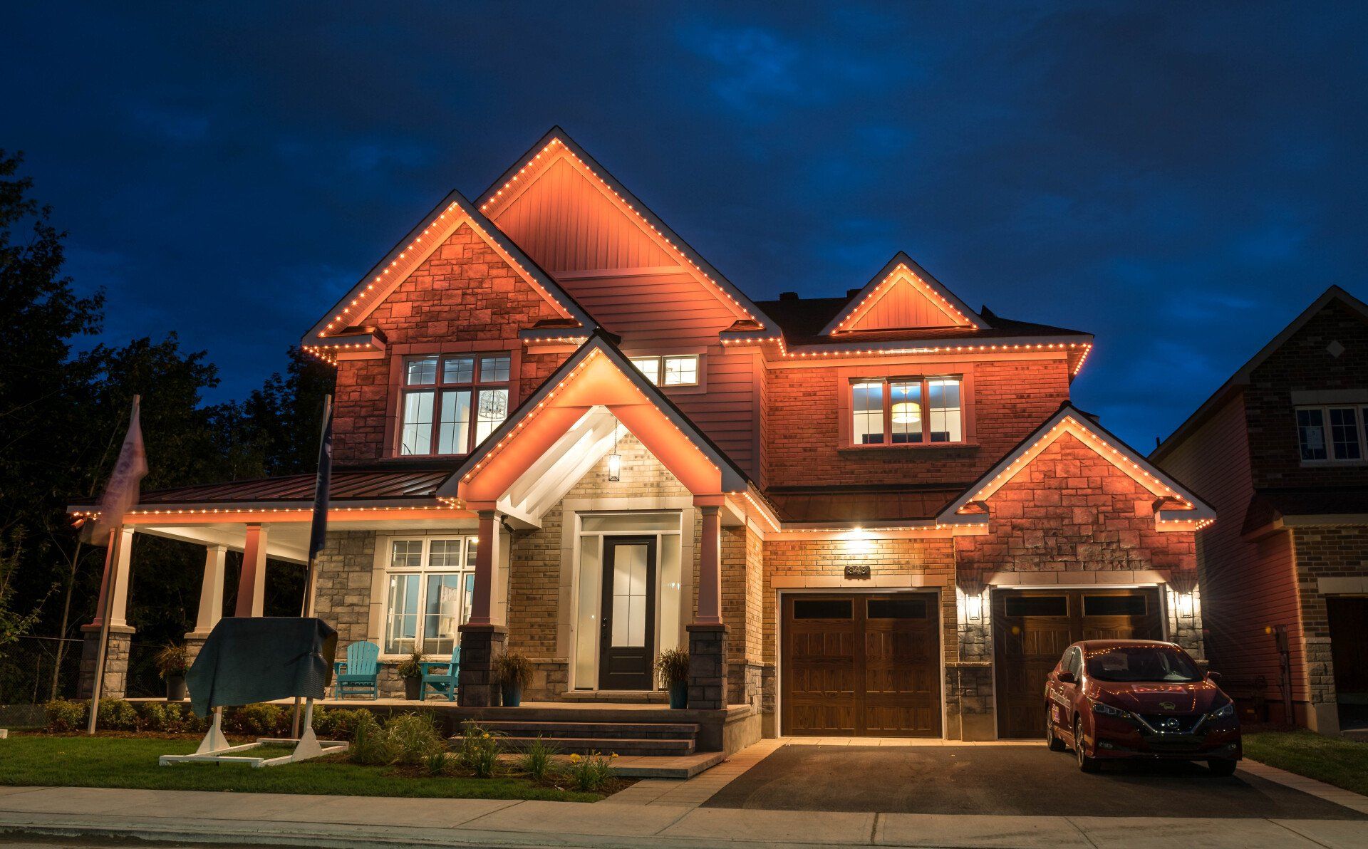 A large brick house is lit up at night with a car parked in front of it.