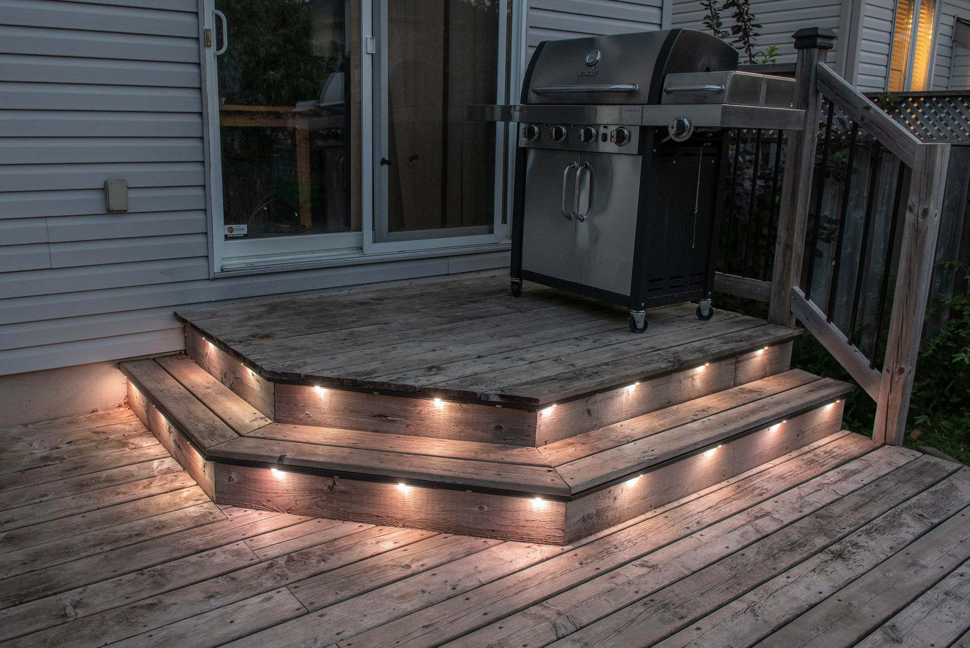 A grill is sitting on a wooden deck with lights on the steps.