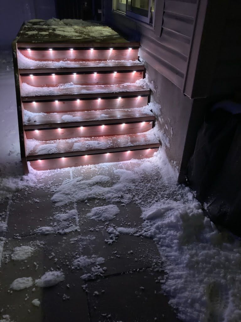 A set of stairs with lights on them are covered in snow.