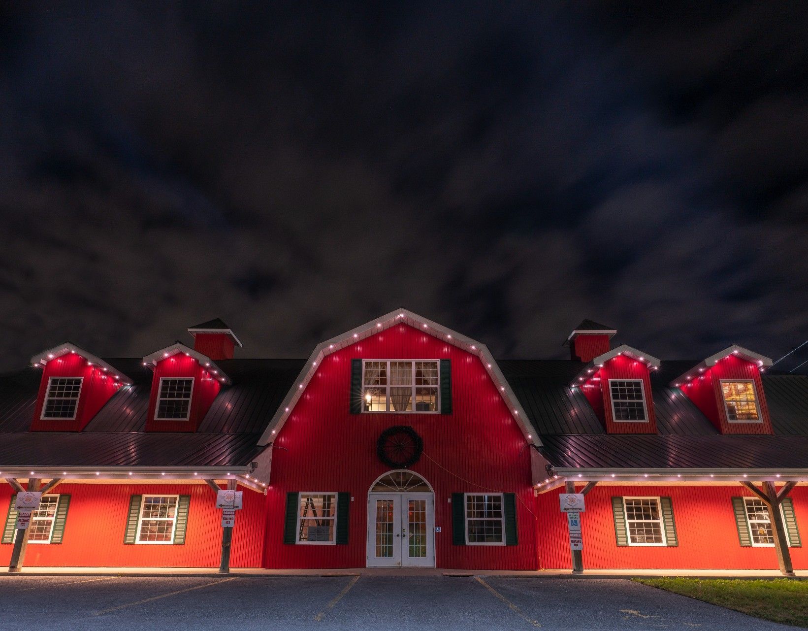 A large red barn is lit up with christmas lights at night.