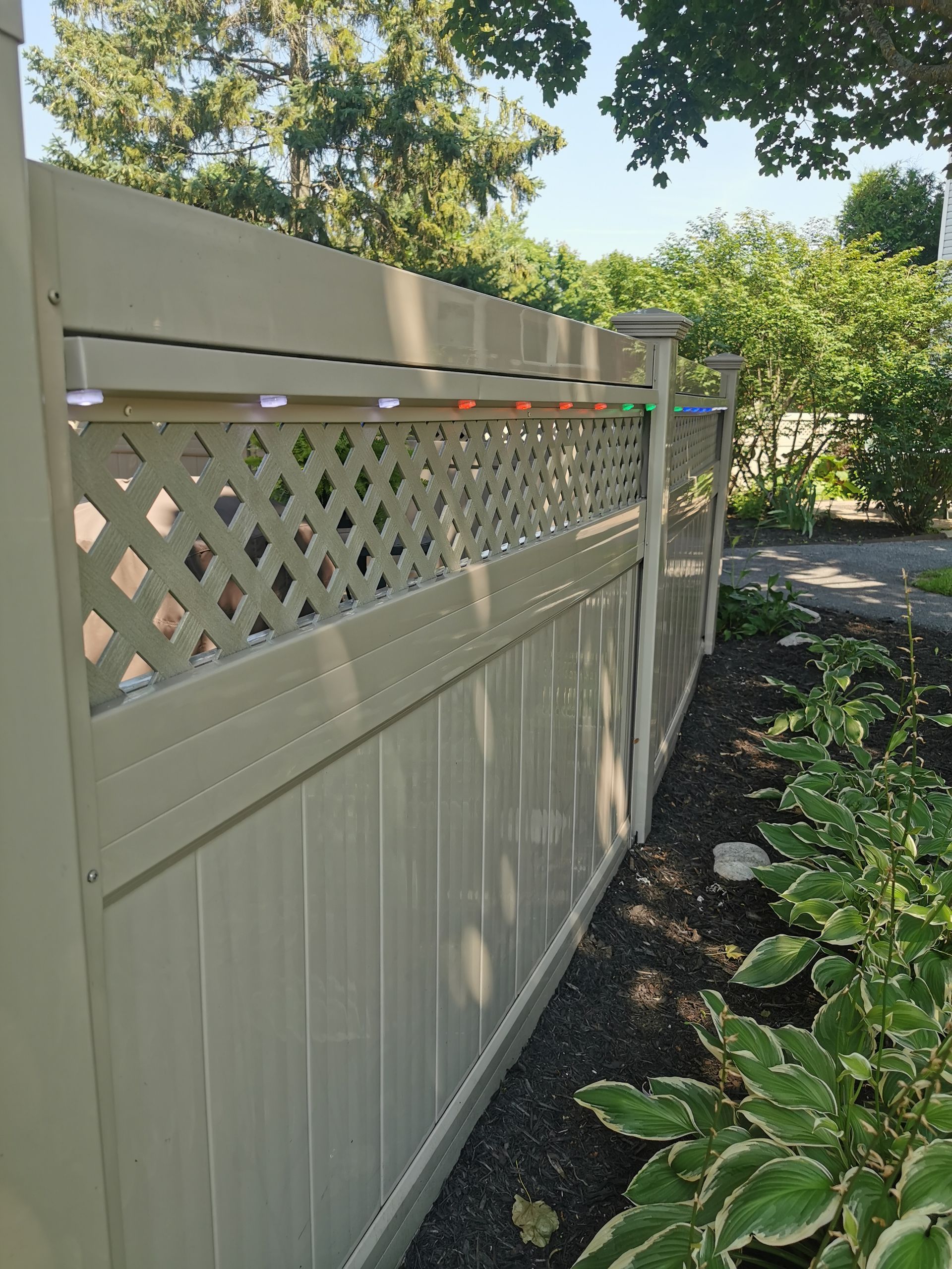 A white fence with a lattice design is surrounded by trees and bushes.