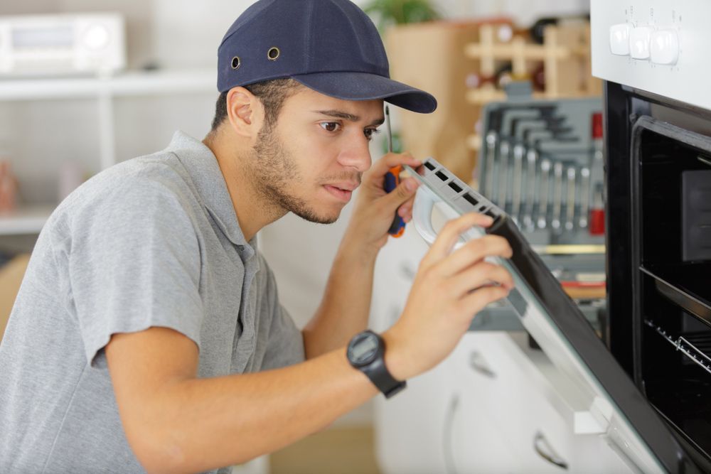 Man is Fixing an Oven With a Screwdriver in a Kitchen — Seal Tite in Ballina, NSW