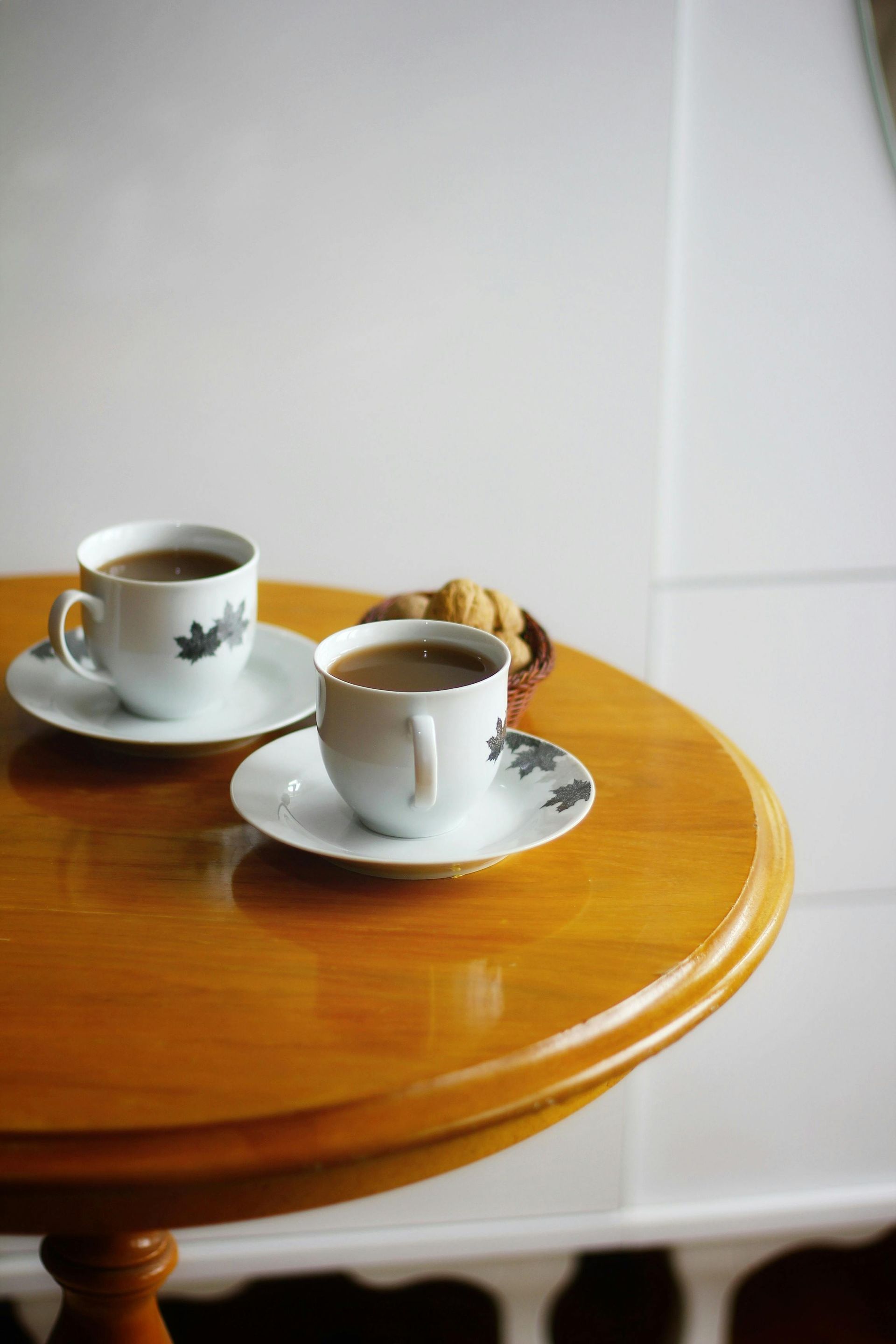 Two cups of coffee on saucers, with pastries, sit on a wood table.