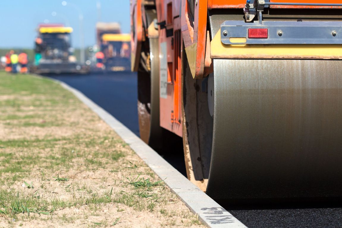 A roller is rolling asphalt on the side of a road.