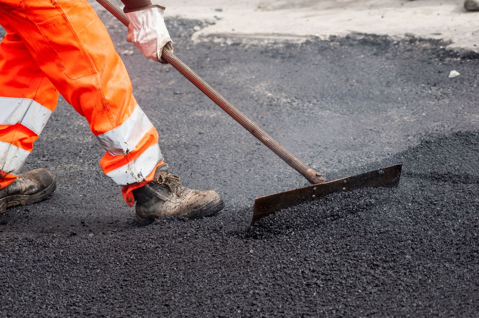 A man is raking asphalt on a road with a rake.