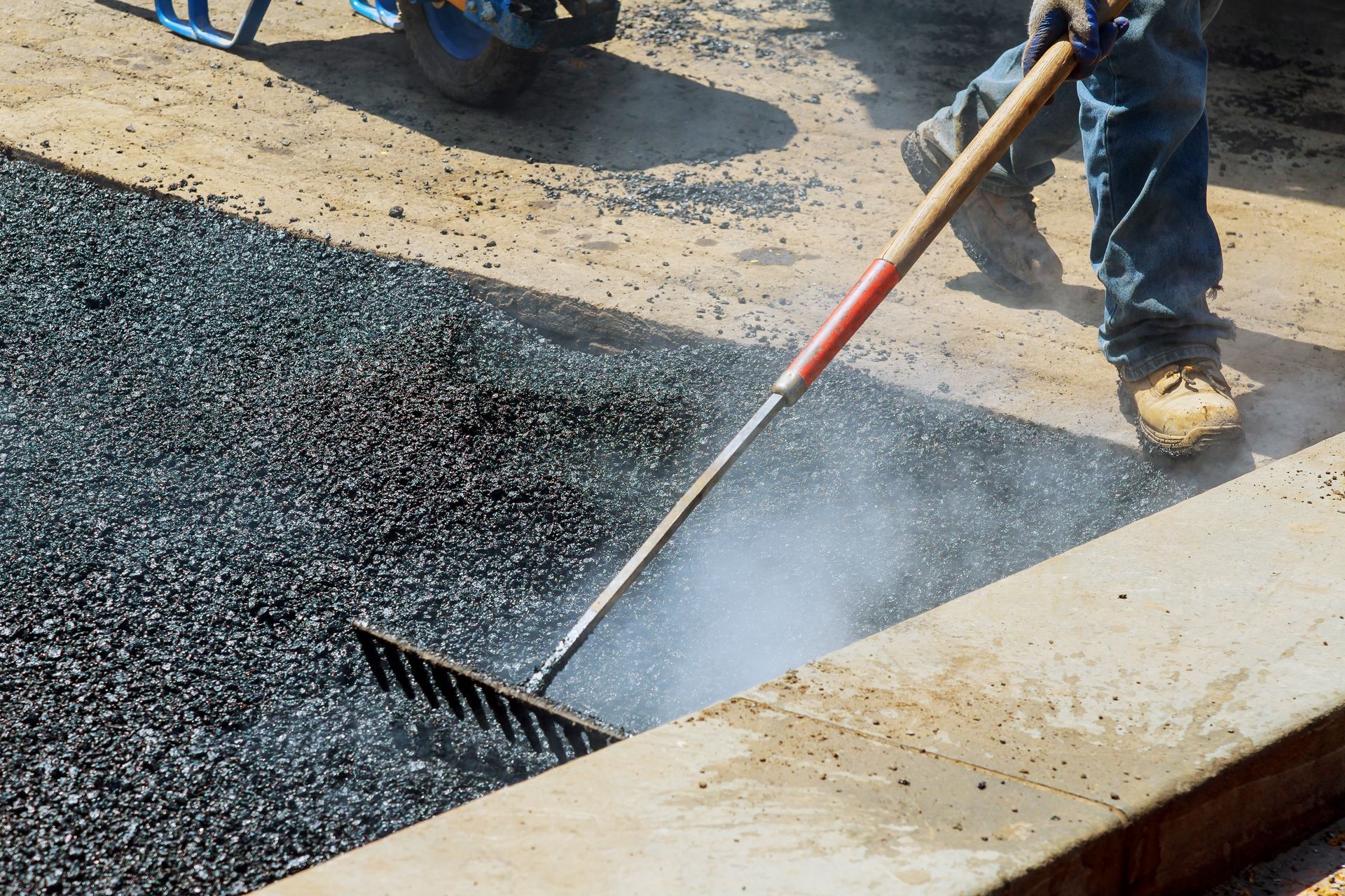 A man is raking asphalt on a sidewalk with a rake.