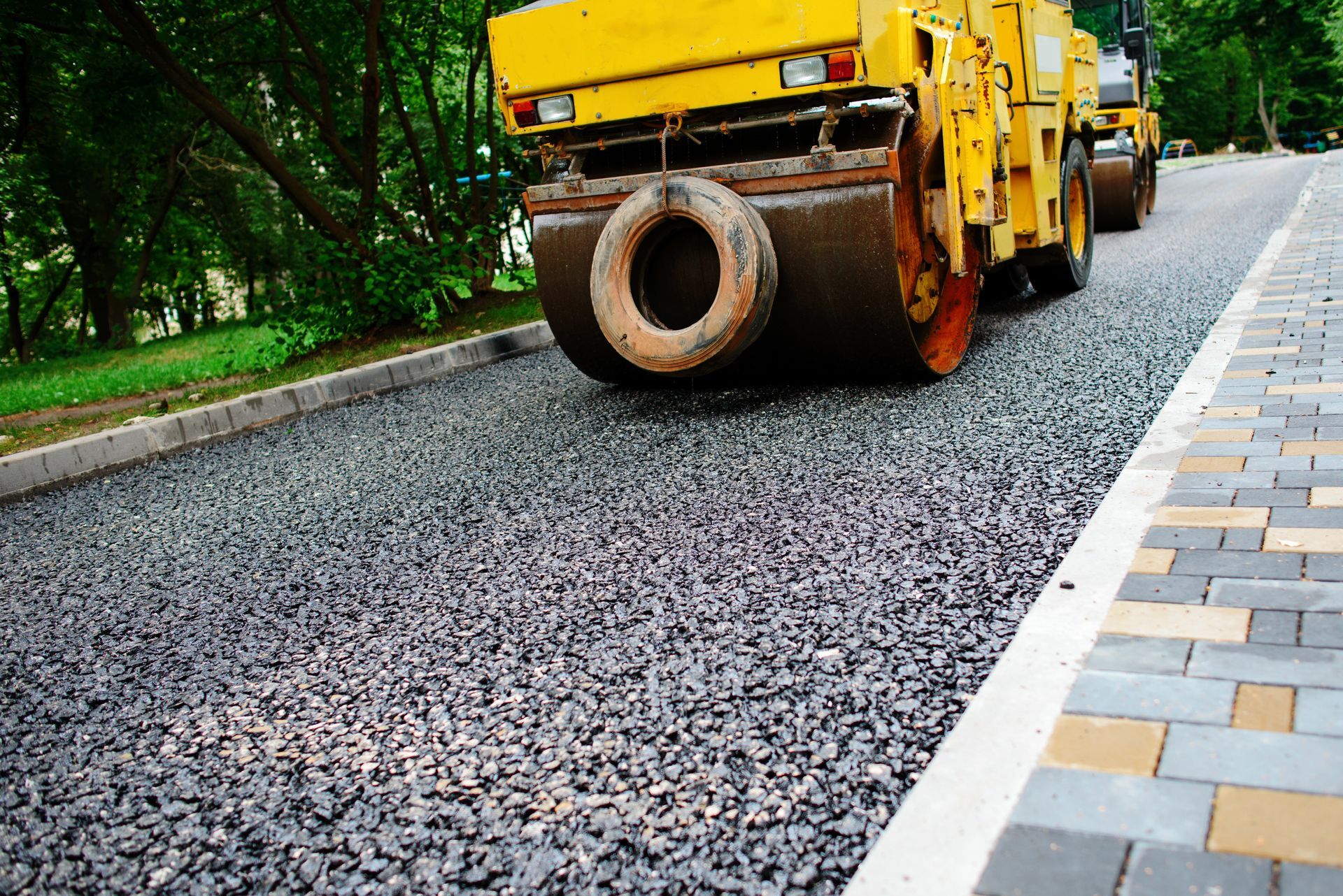 A yellow roller is rolling gravel on a road.