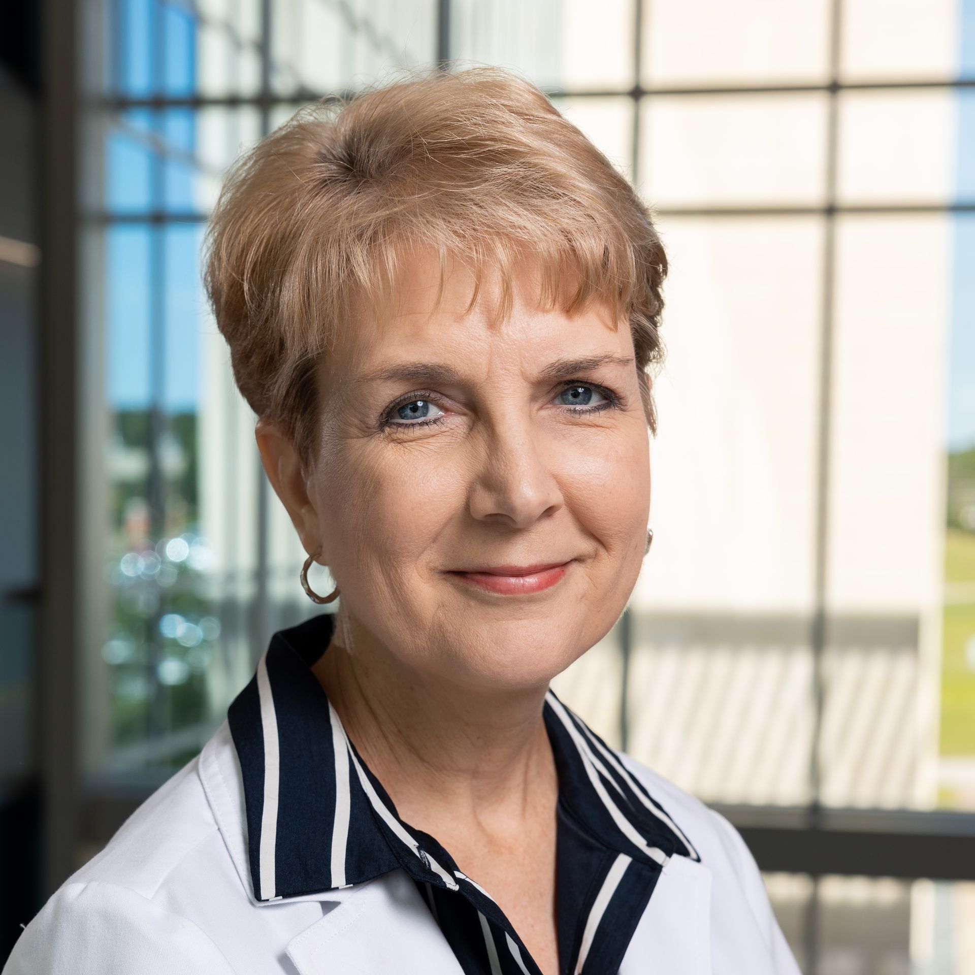Woman with long dark hair, smiling, wearing a red top and pearl necklace.