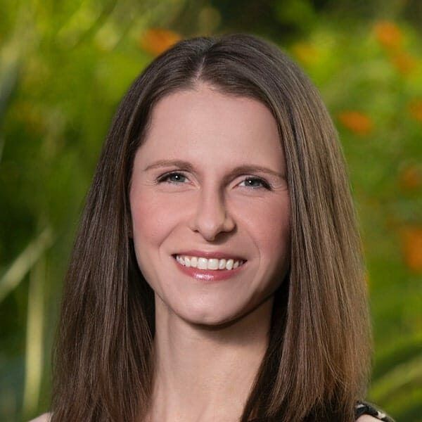 Woman with brown hair, smiling, wearing a black and white patterned top, outdoors.