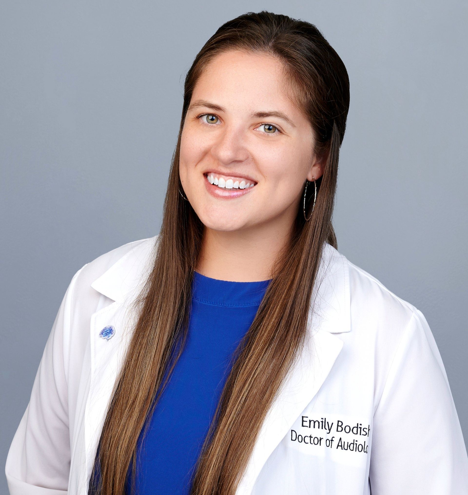 Woman with long dark hair, smiling, wearing a red top and pearl necklace.