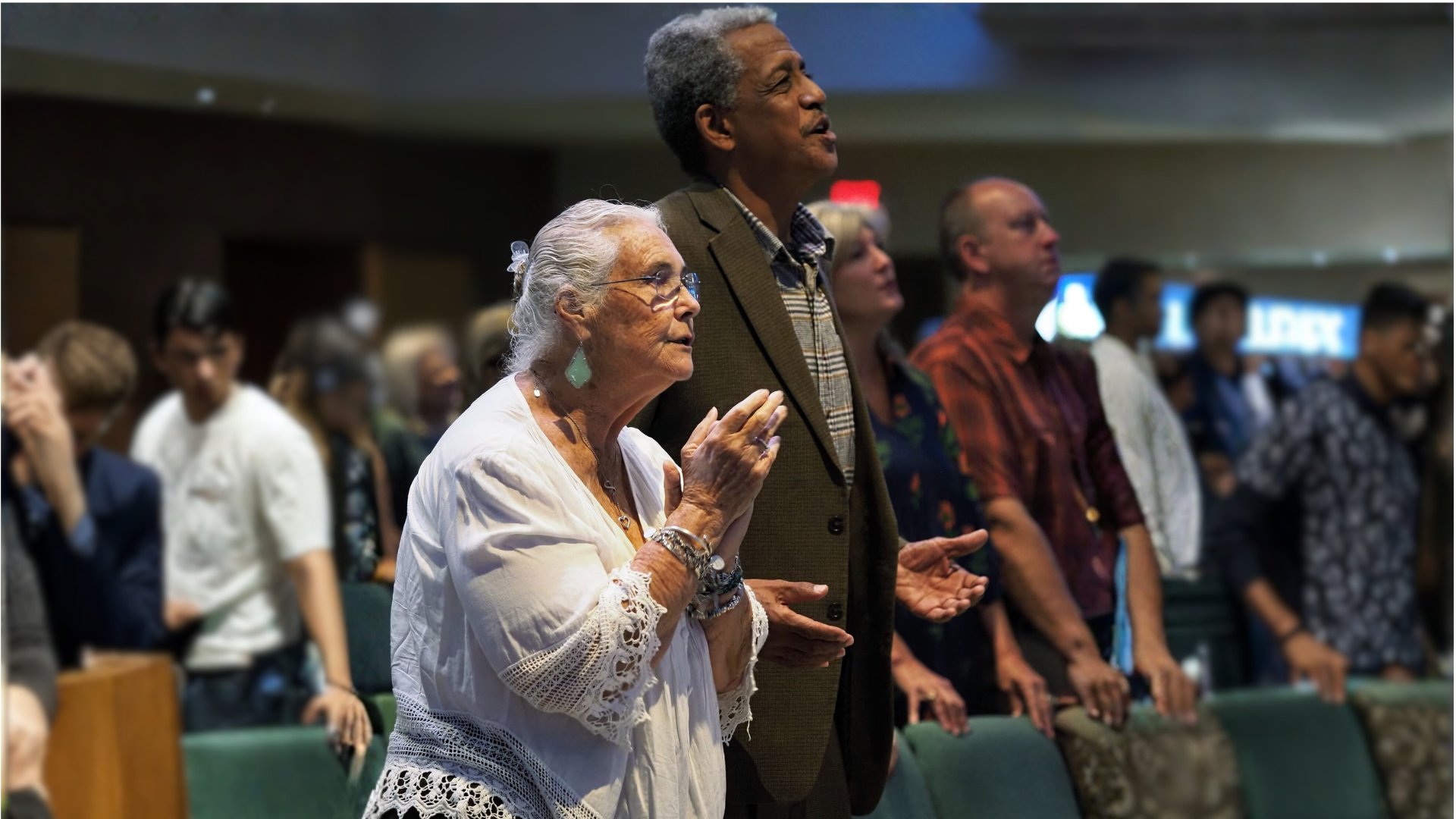Choir performing onstage for an audience. Singers in black, some with red scarves, illuminated by stage lights.