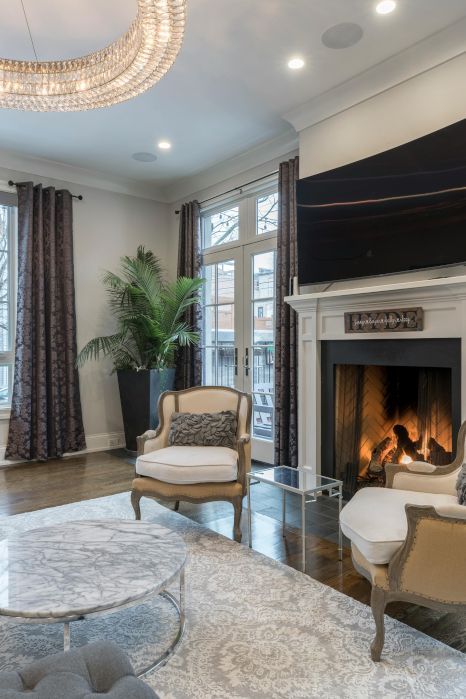 A living room with a fireplace , chairs , a coffee table and a flat screen tv.