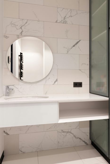 A bathroom with a sink , mirror and marble tiles.