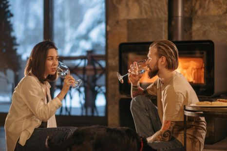 A man and a woman are drinking wine in front of a fireplace.