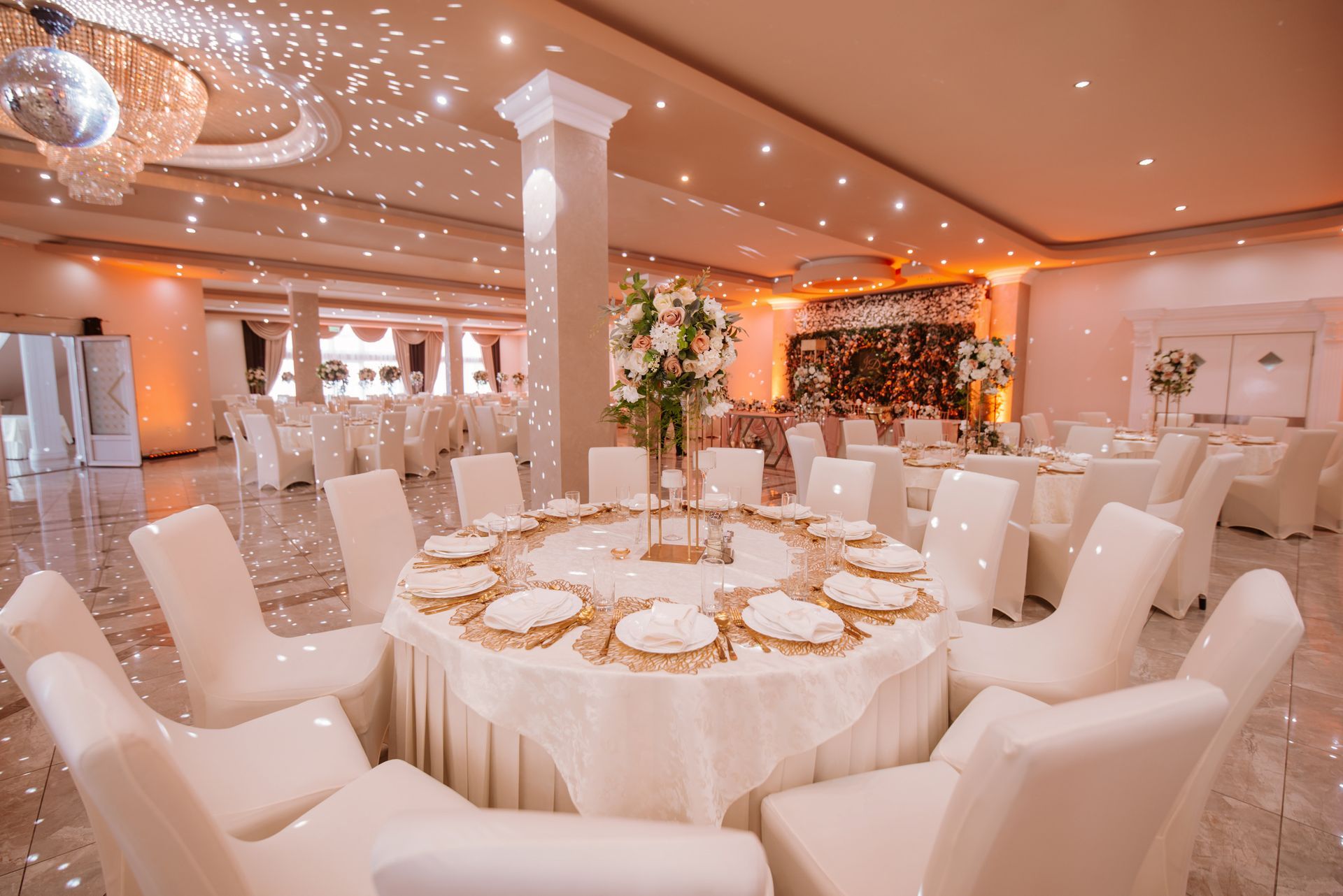 Elegant banquet hall with round tables set for a celebration, white and gold decor, star-like ceiling lights.