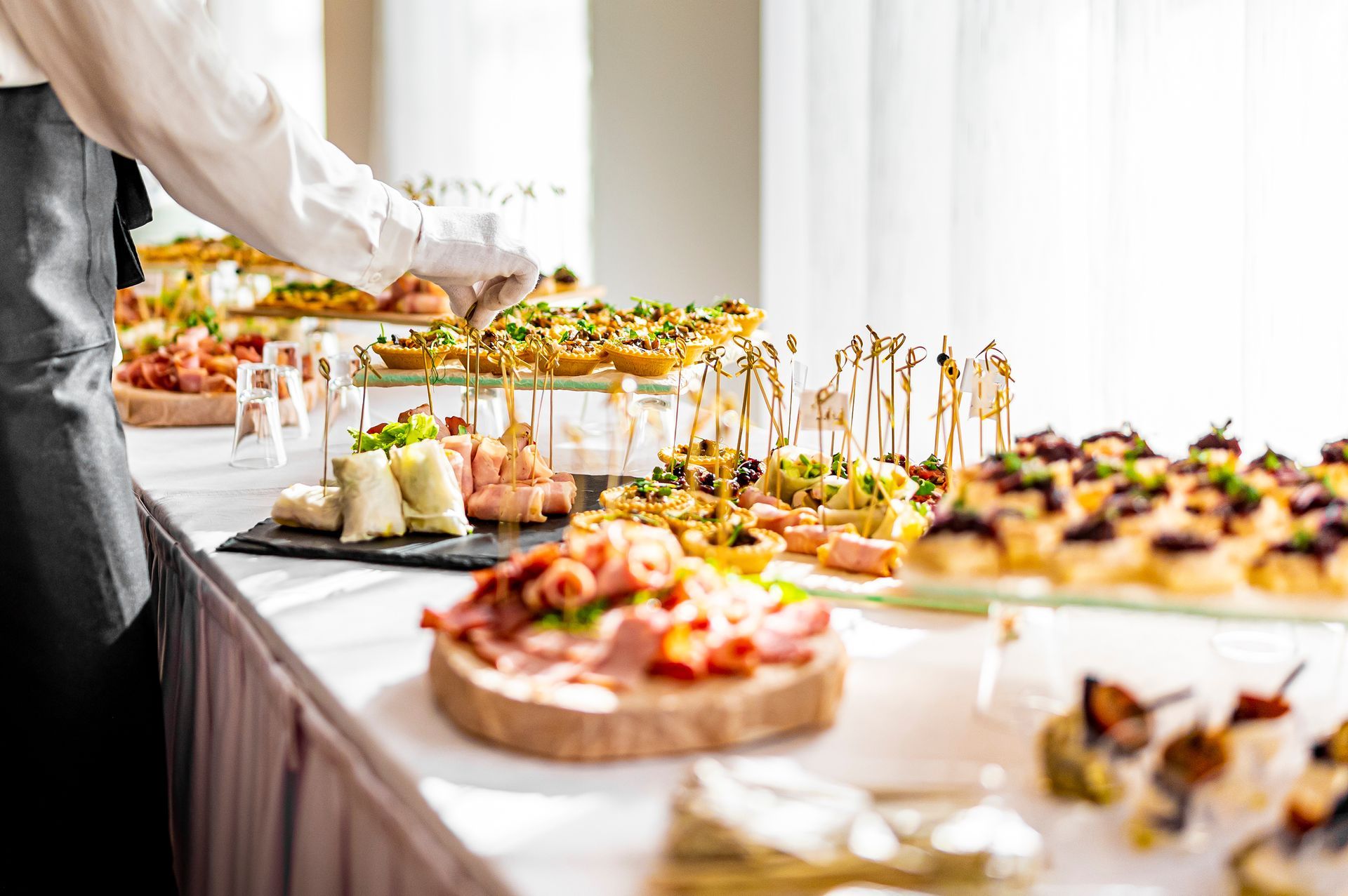 Caterer arranging hors d'oeuvres on a buffet table with a variety of appetizers, in a well-lit setting.