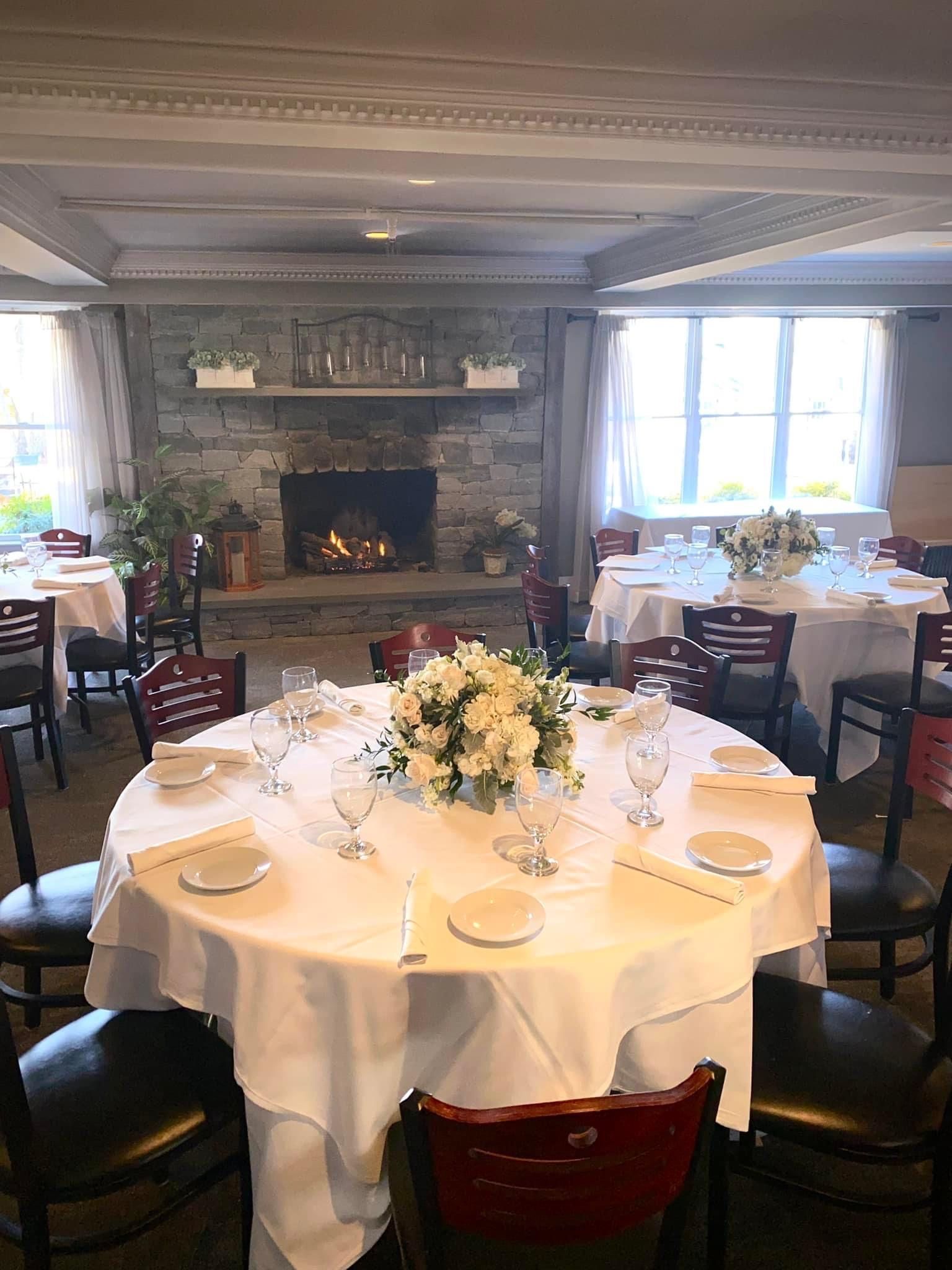 Elegant dining room with round tables set for a meal, fireplace, and windows.