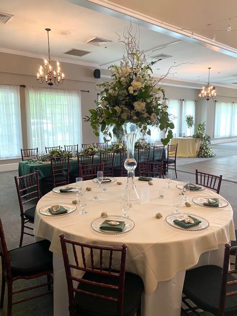 Elegant wedding reception with round tables, tall floral centerpiece, and chandeliers.