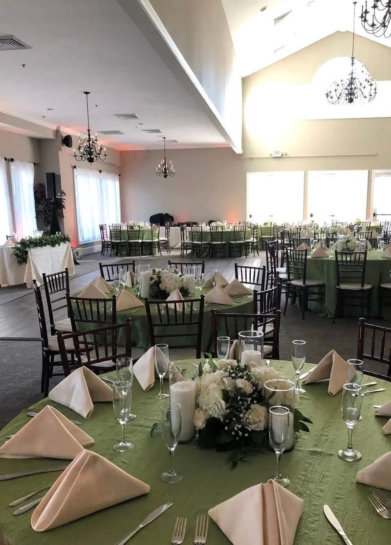 Wedding reception hall set with green tablecloths, white floral centerpieces, and place settings.
