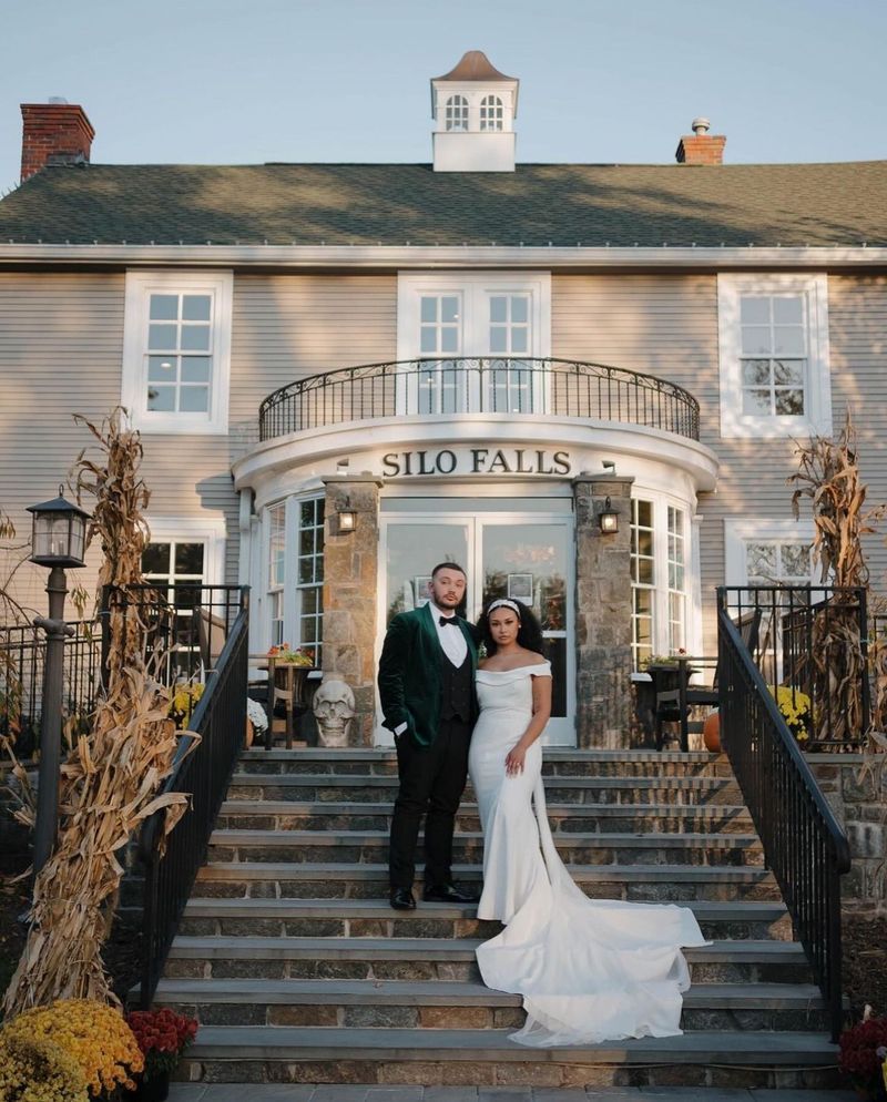 Couple standing on steps in front of Silo Falls building. The man in green suit, woman in white gown.