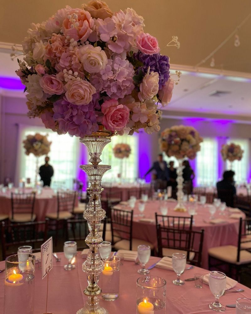 Wedding reception tables with pink linens and floral centerpieces, lit by candles, in a ballroom.