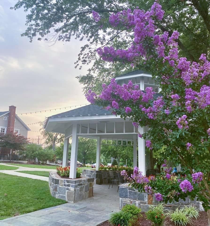 Gazebo with purple flowers, stone path, and grassy area under a cloudy sky.