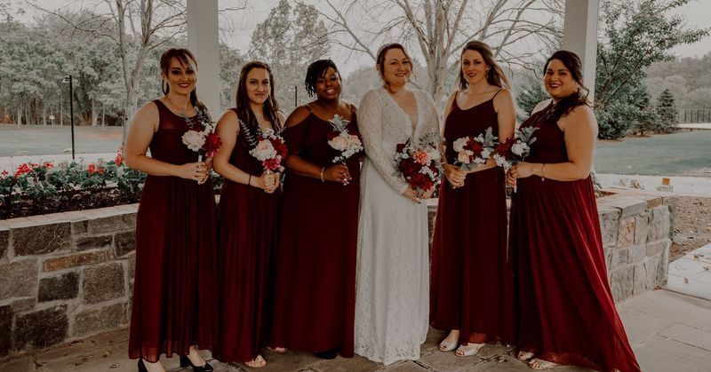 Bride and bridesmaids in burgundy dresses pose outdoors, holding bouquets.