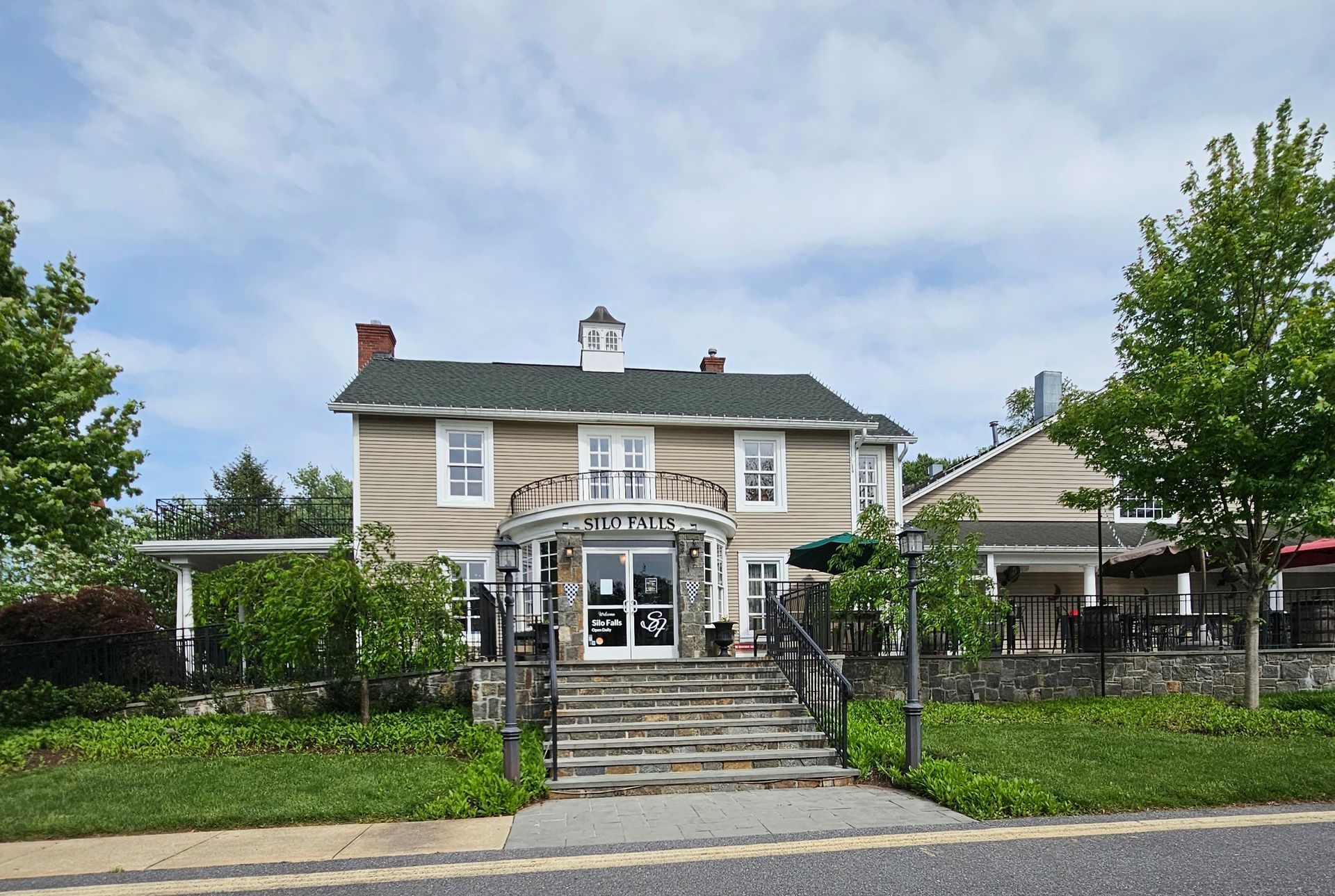 Two-story beige building with stone steps, a covered entryway, and a green roof.