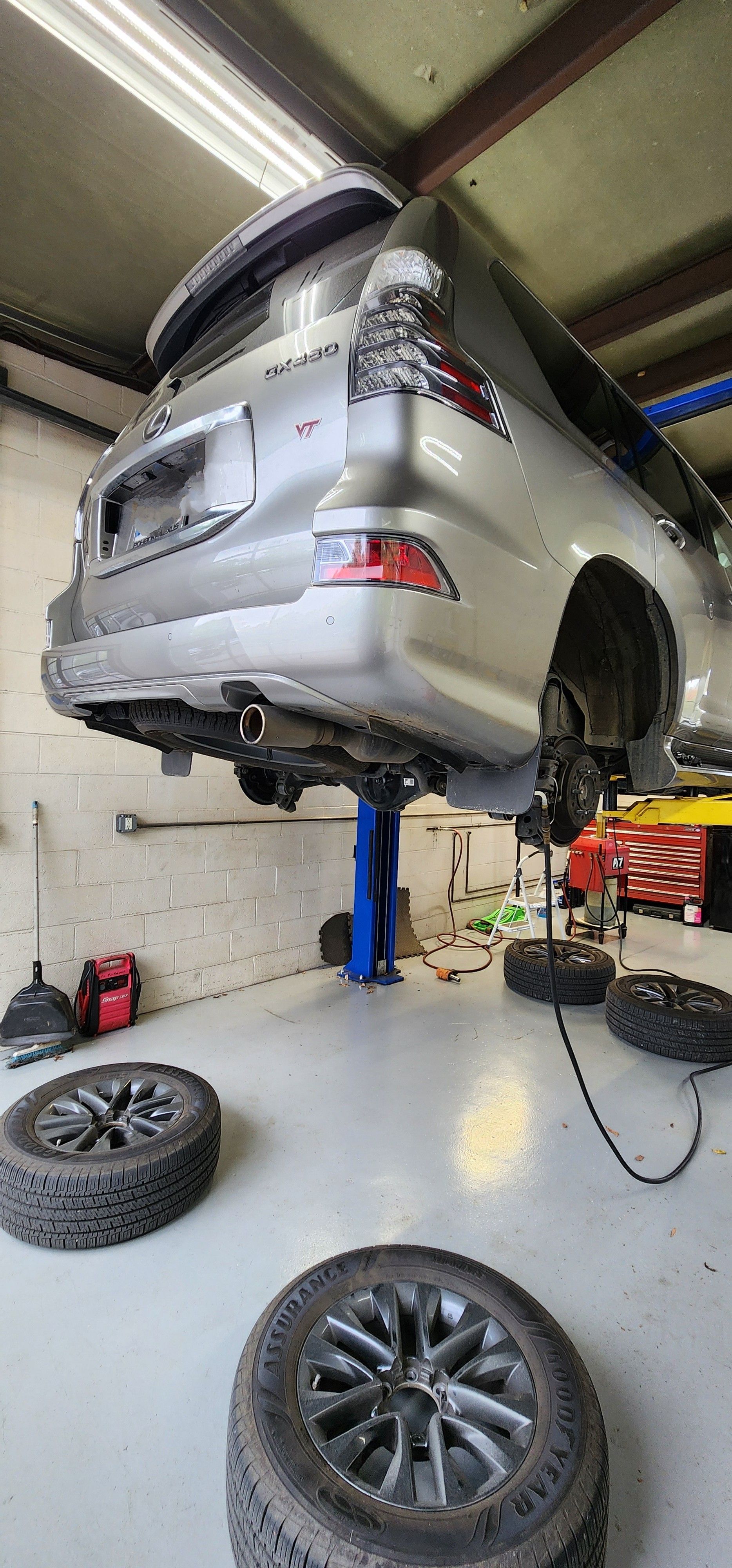 A silver SUV on a lift in a garage, with tires removed and scattered on the floor. | Ish Auto Clinic