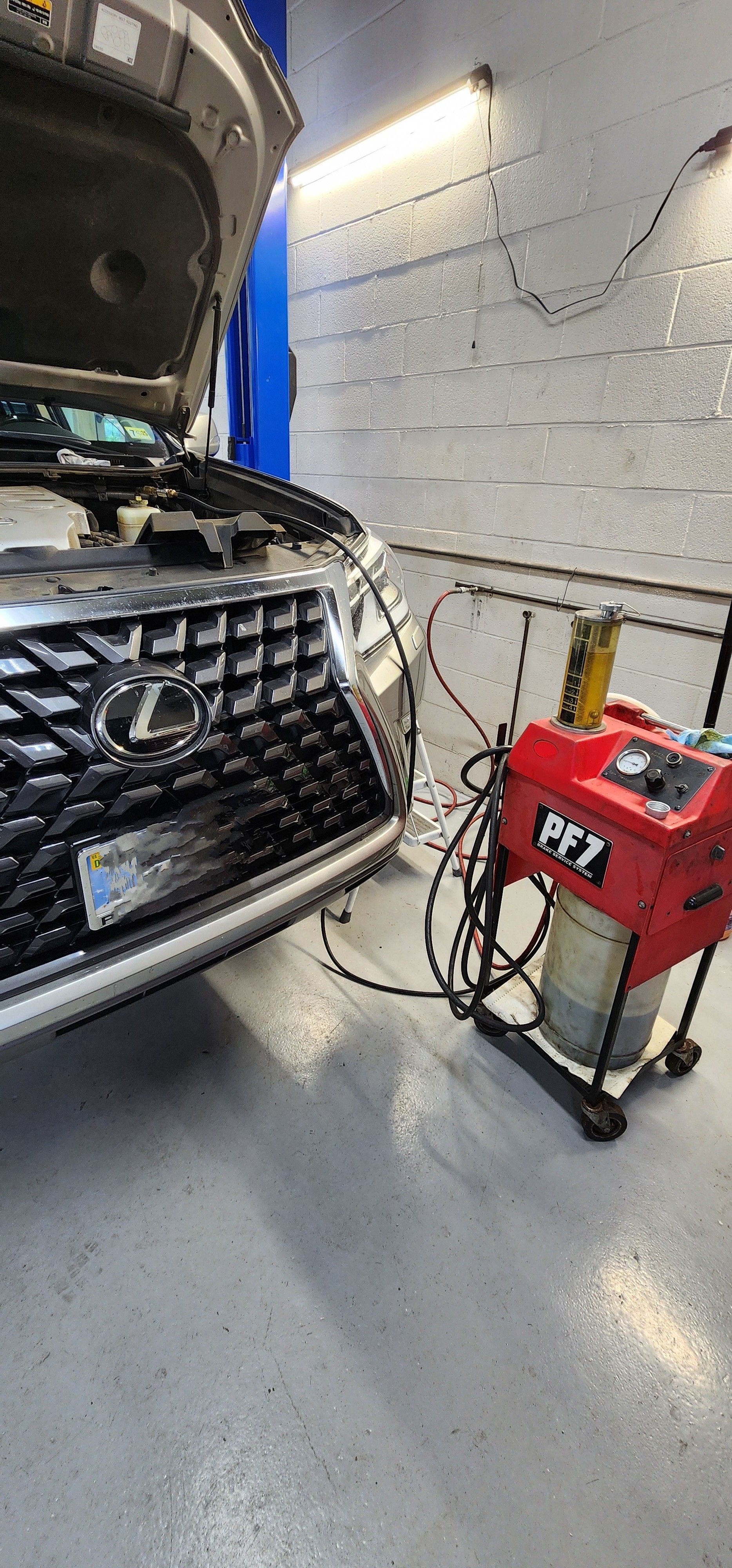 A car with open hood in a repair shop, being serviced by a red machine with hoses. | Ish Auto Clinic