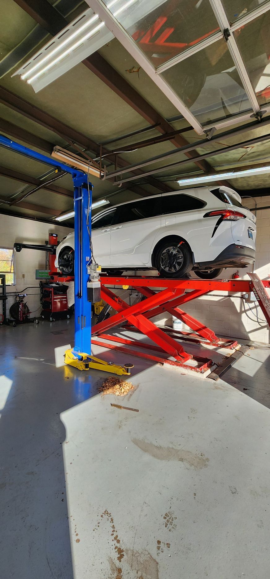 A white car on a red hydraulic lift in a garage. A mechanic lifts the car for service. | Ish Auto Clinic