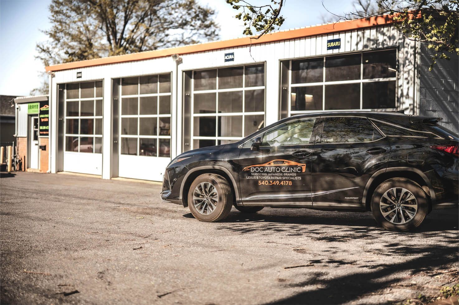 A black SUV parked outside a white garage with three bays. | Ish Auto Clinic