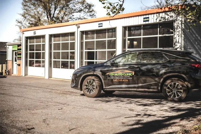 A black SUV parked outside a white garage with three bays. | Ish Auto Clinic