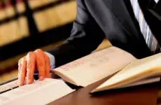 A man in a suit and tie is sitting at a table reading a book.